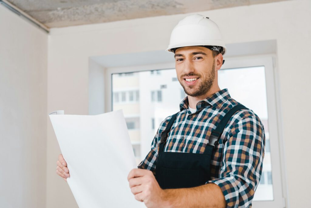 cheerful handyman smiling while holding blueprint